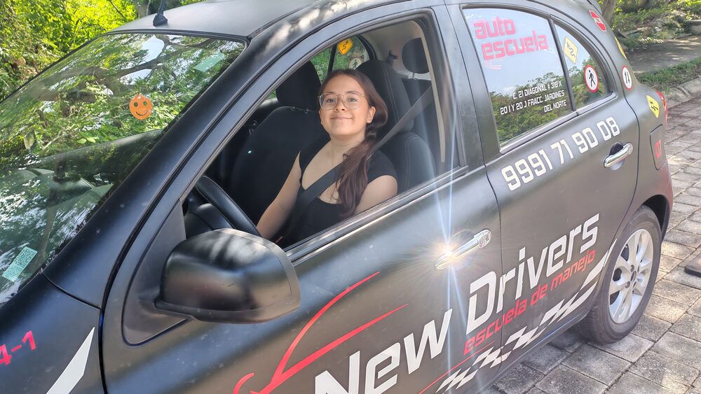 Alumna de New Drivers con lentes sonriendo al volante del auto de práctica