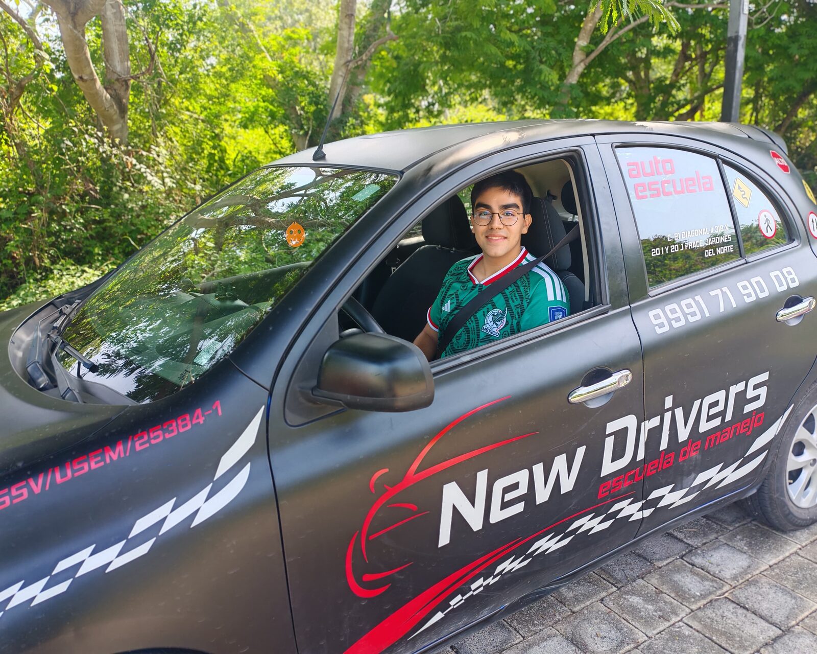 Alumno de New Drivers sonriendo al volante de un auto de práctica identificado con el logo de la escuela